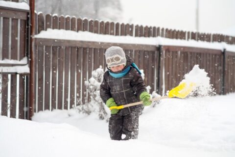 kid shoveling snow by fence