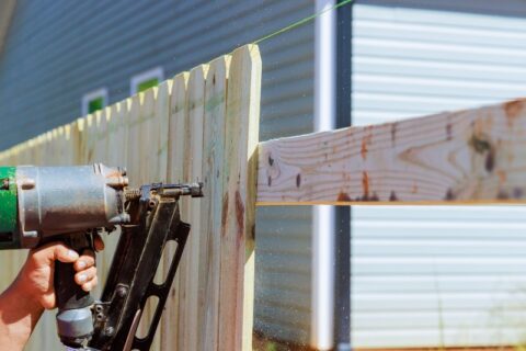 Man builds sections of nailing a wooden fence around his yard out planks using air nail gun in Chicagoland, IL
