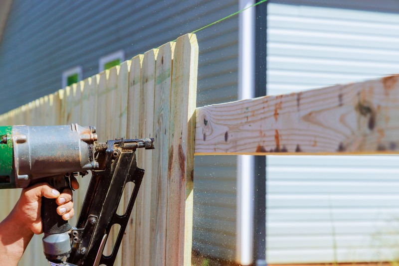Man builds sections of nailing a wooden fence around his yard out planks using air nail gun in Chicagoland, IL