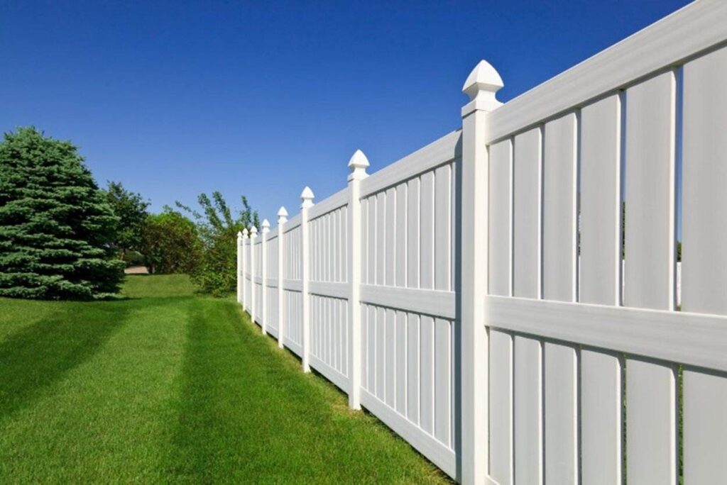 White vinyl fence with post caps along green lawn under blue sky, Chicago, IL